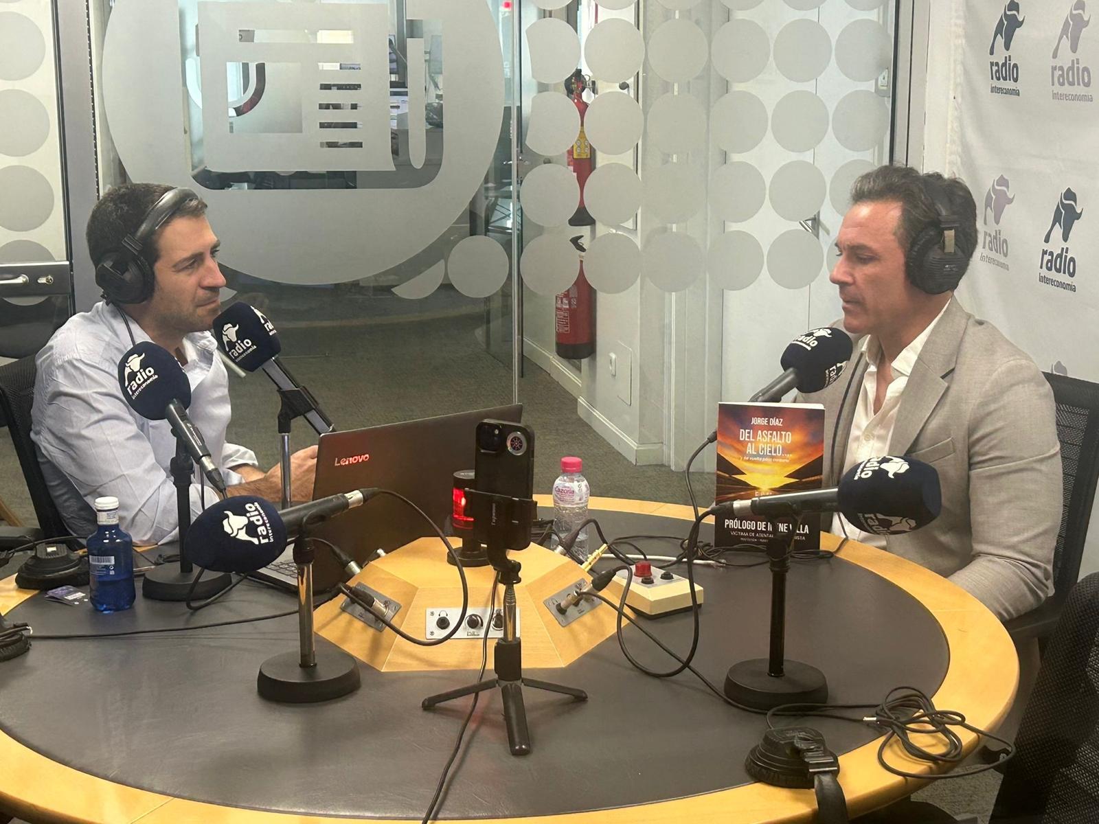 Jorge Díaz con auriculares en una entrevista en Radio Intereconomía, su libro 'Del Asfalto al Cielo' sobre la mesa
